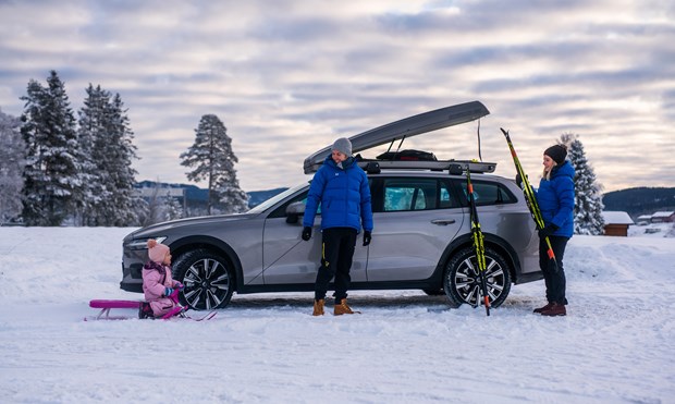 En familie med mor, far og barn står foran en Volvo med skiboks på taket. 